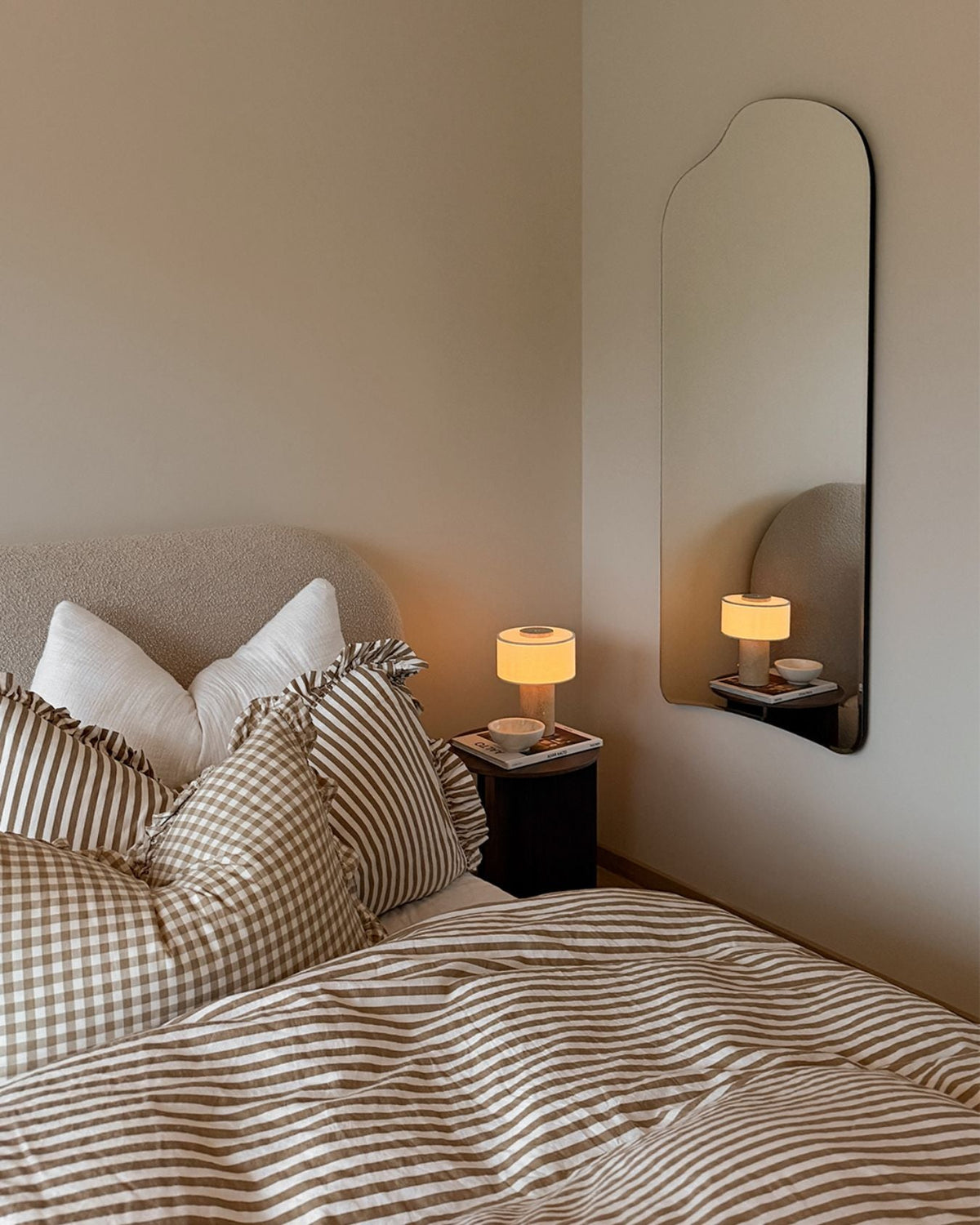 Oriel Travertine Portable Lamp glowing beside striped bedding
