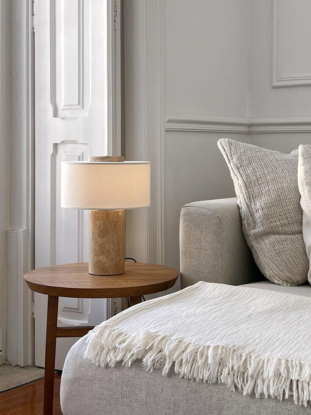 Oriel Travertine Table Lamp on a round table beside a sofa