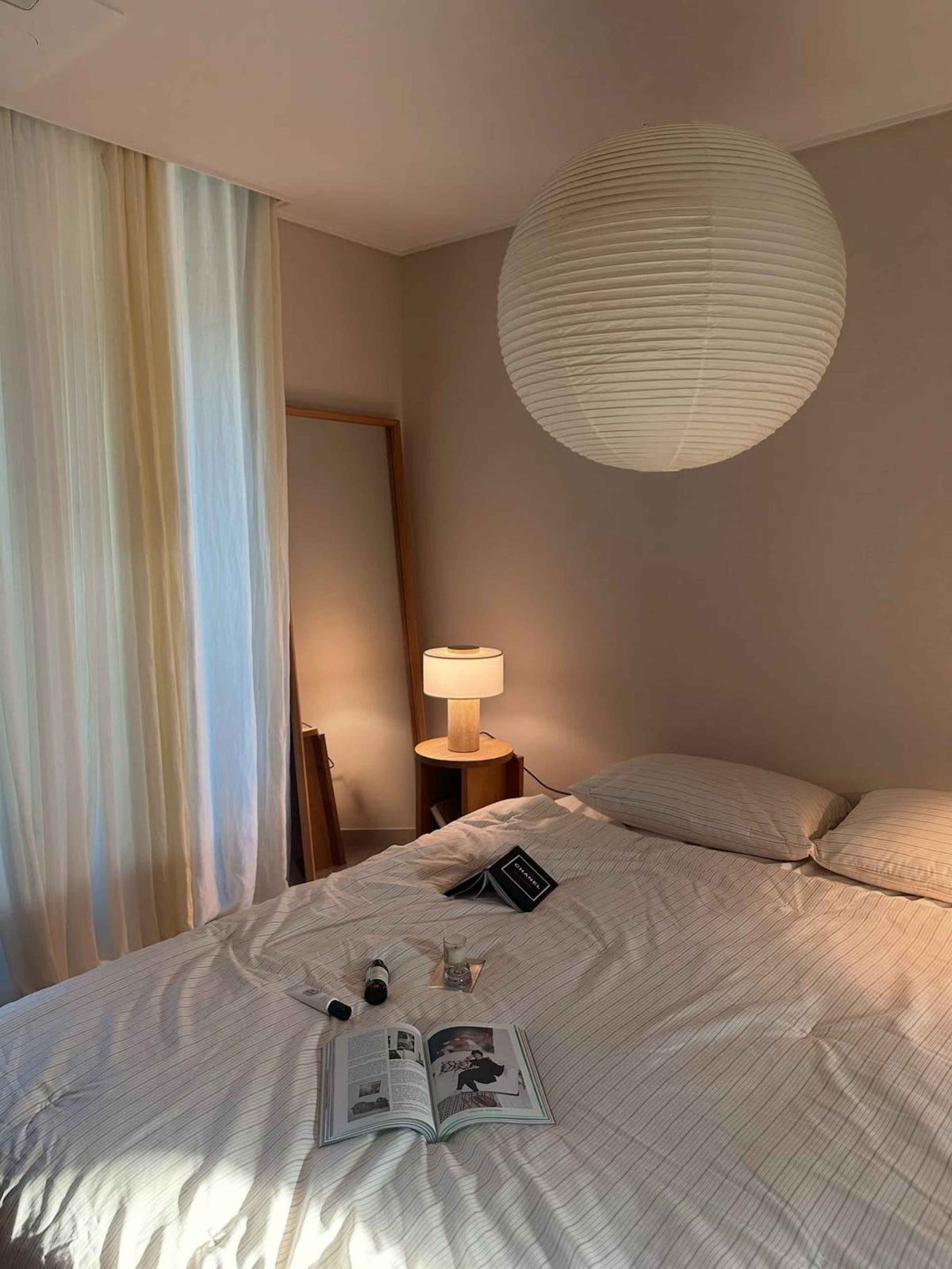 Oriel Travertine Table Lamp glowing beside a bed beneath a round pendant